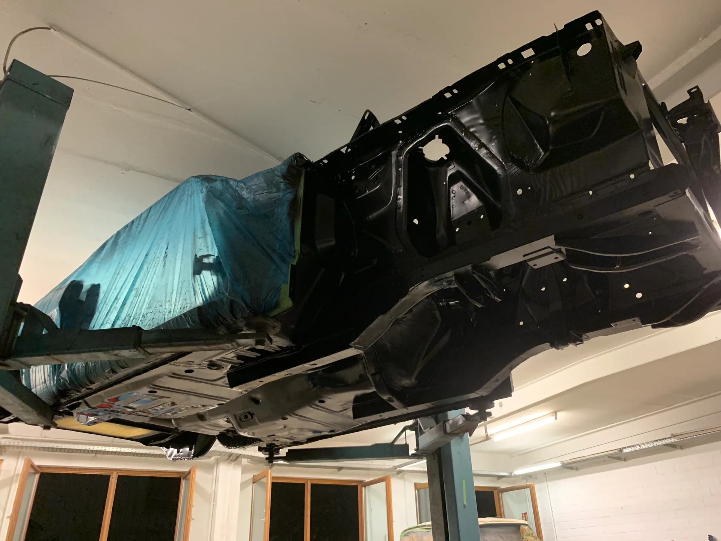 Komplett zerlegte Fahrzeugkarosserie auf der Hebebühne, in dunkler Grundierung, für die Lackierung vorbereitet.