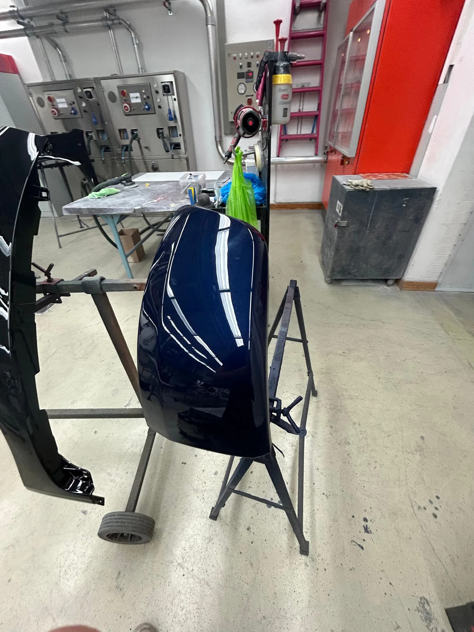 Frisch lackierter Kotflügel in dunkelblauem Metallic auf einem Lackierständer, die Deckenbeleuchtung spiegelt sich in einer geschlossenen Linie.