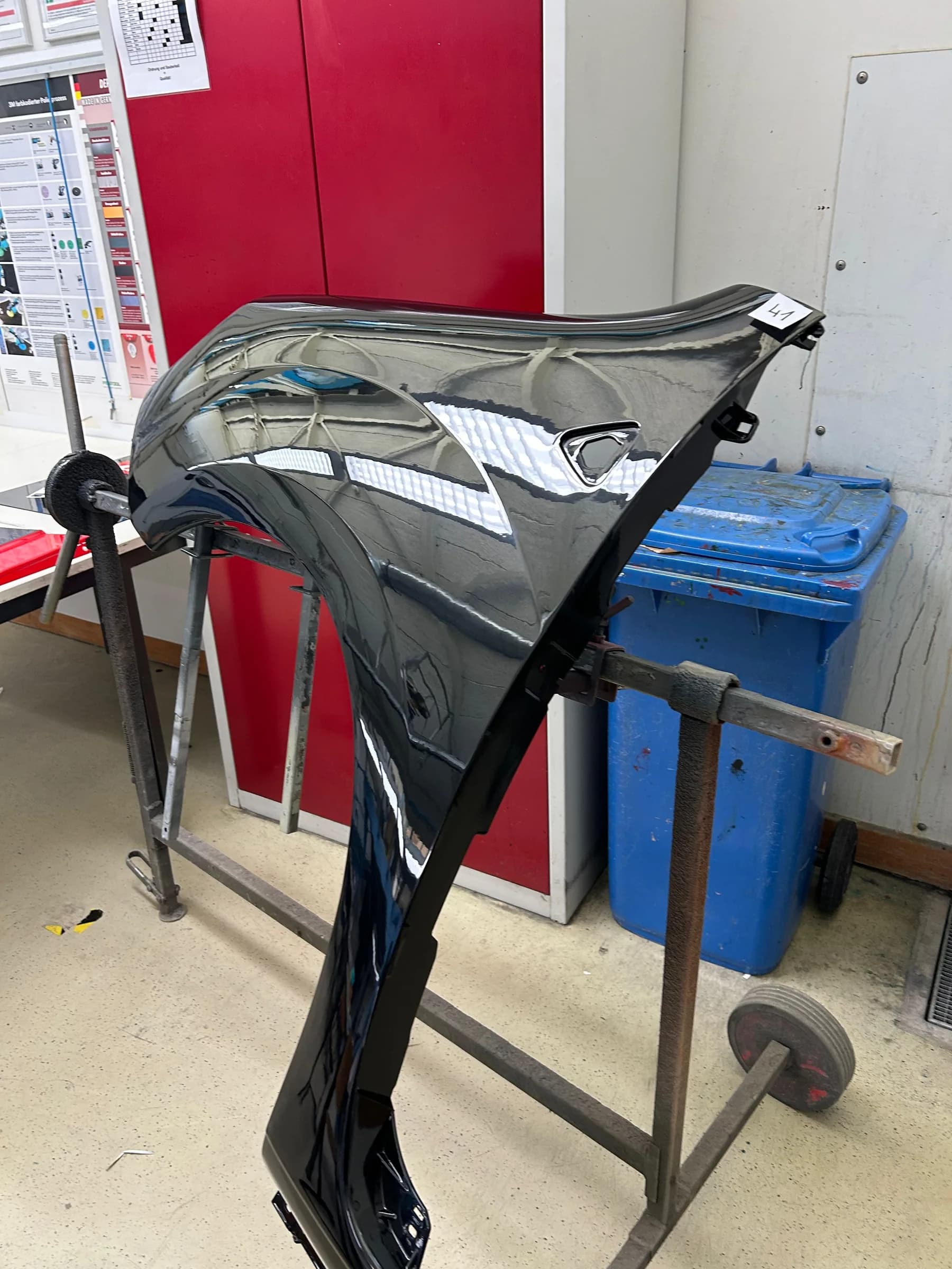 Lackierte Motorhaube auf einem Rollständer in der Werkstatt, die Oberfläche wirft ein klares Spiegelbild.
