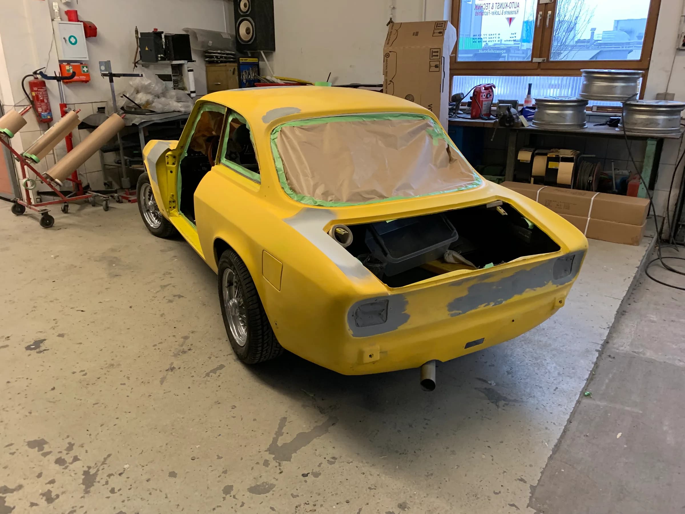 Gelbes klassisches Coupé von Alfa Romeo in der Werkstatt, Scheiben und Heckpartie für die Weiterarbeit abgeklebt.