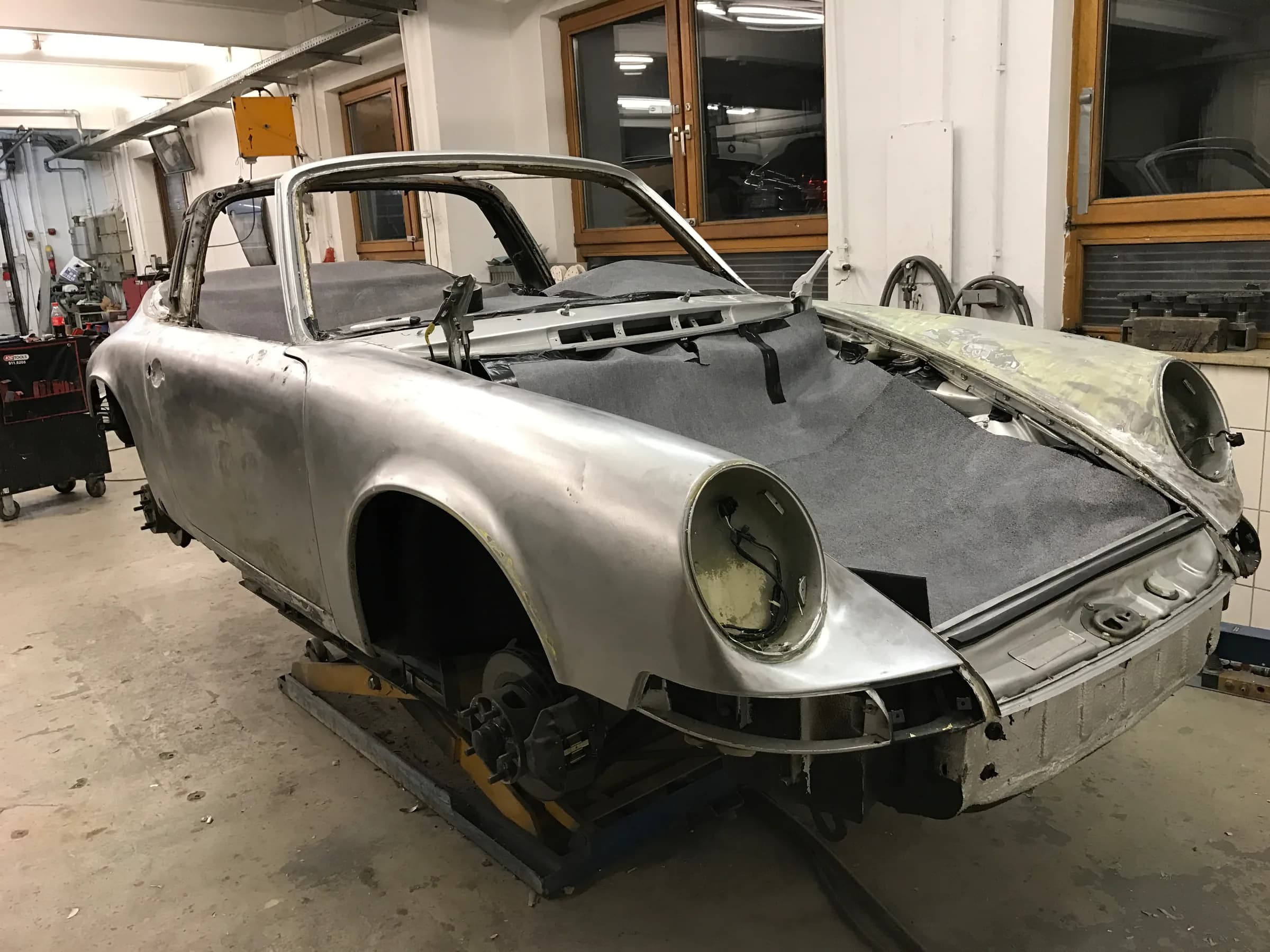 Karosserie eines frühen Porsche 911, vollständig entlackt bis aufs blanke Metall, ohne Türen und Hauben auf Böcken in der Werkstatt.