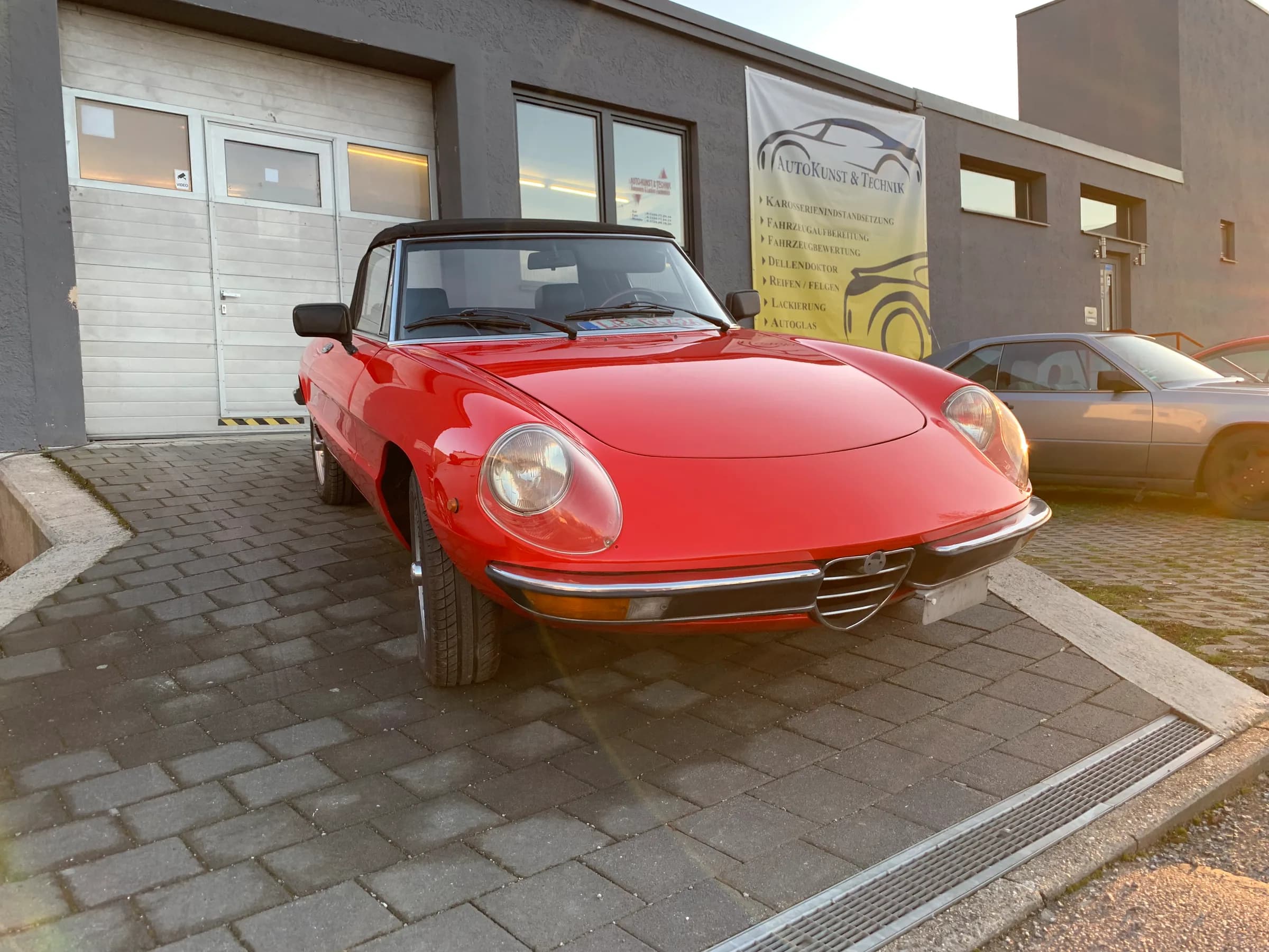 Roter Alfa Romeo Spider nach der Lackierung, fahrbereit auf dem Hof vor der Werkstatt.