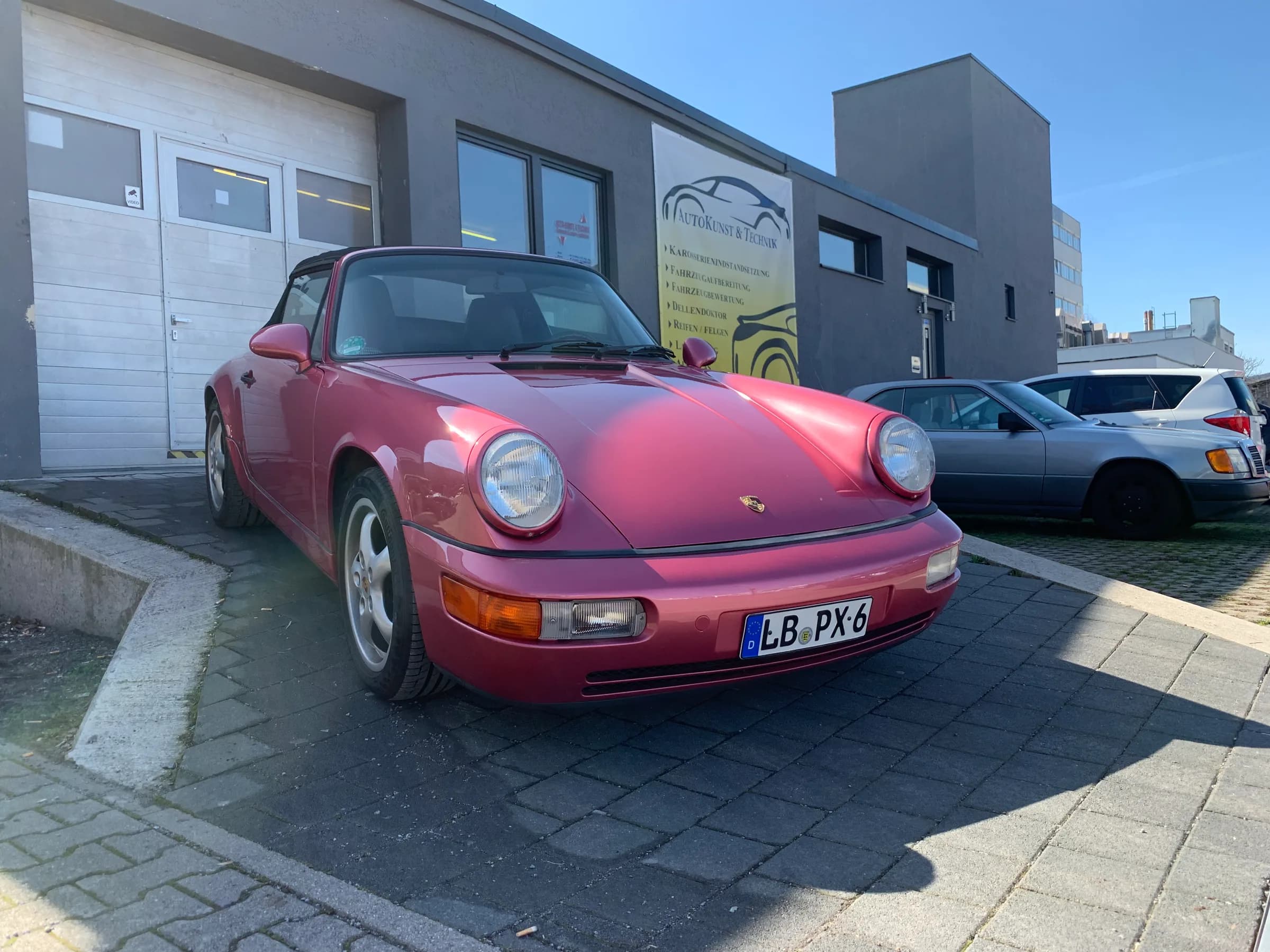 Porsche 911 der Baureihe 964 in kräftigem Pink, fertig lackiert vor der Werkstatt geparkt.