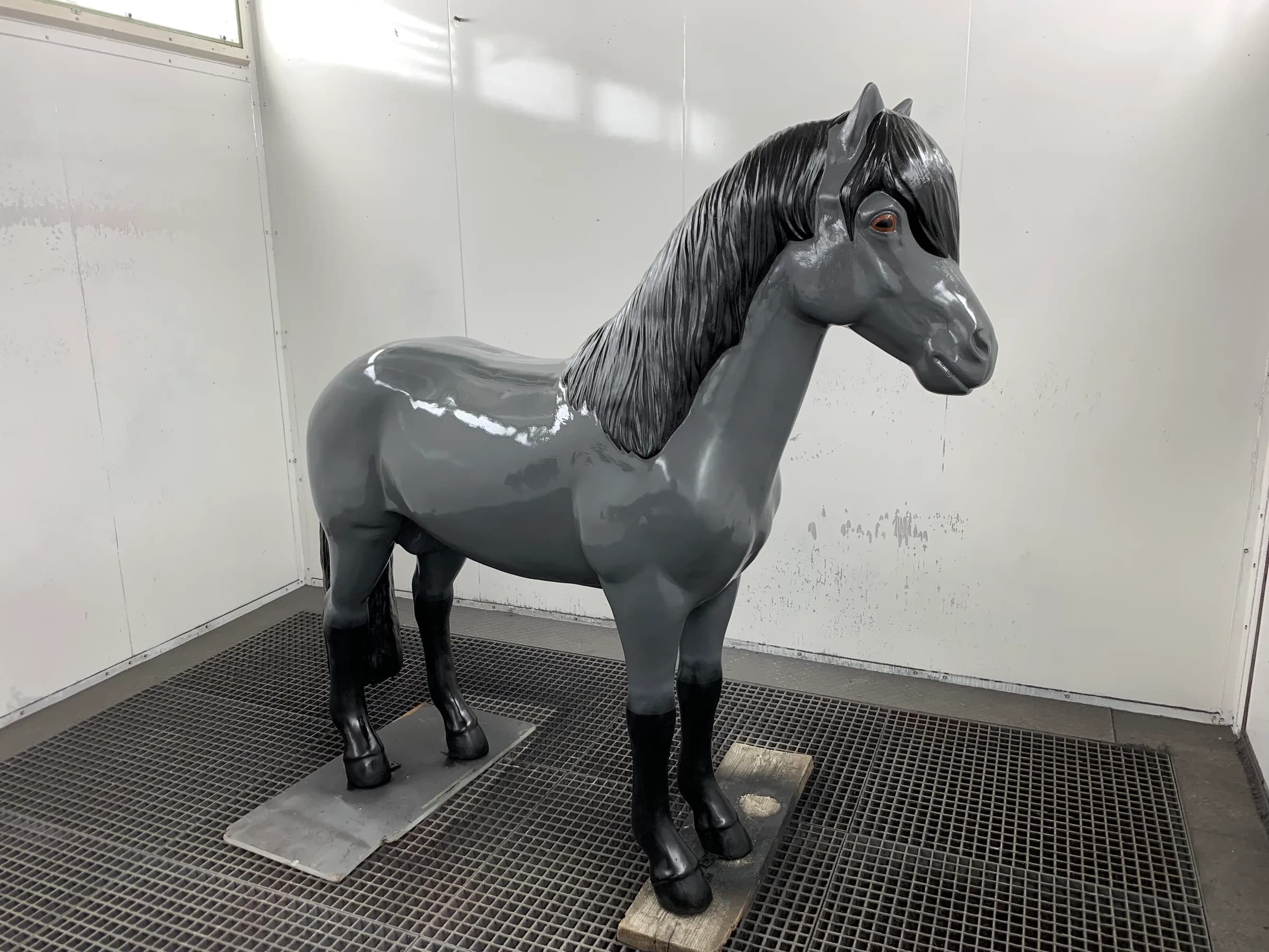 Die fertig lackierte Pferdefigur in der Kabine: grauer, glänzender Körper, schwarze Mähne, schwarze Hufe.