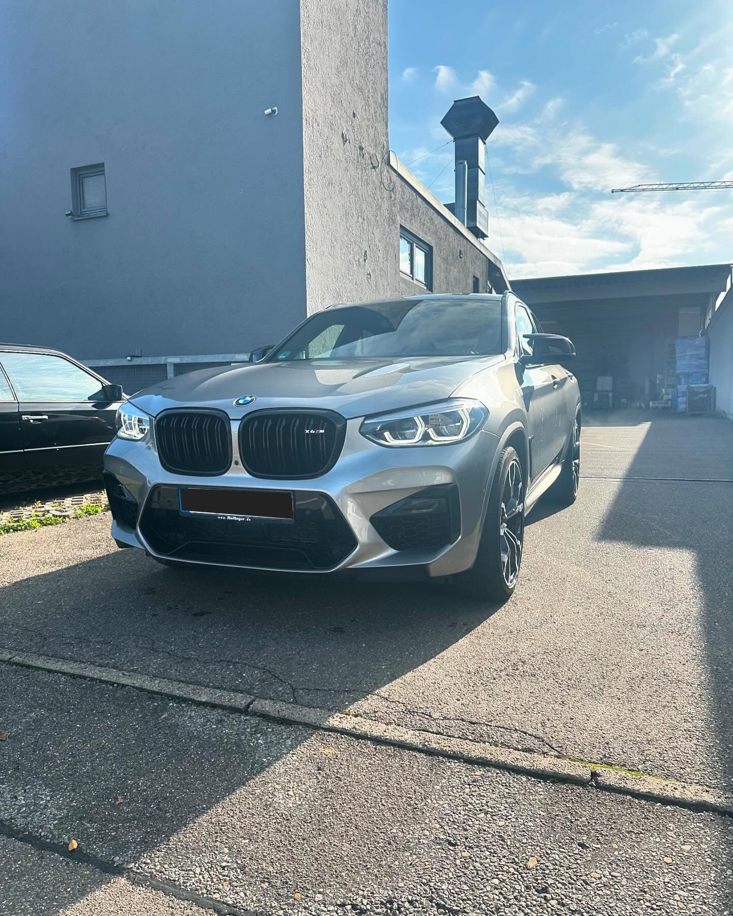 Grauer BMW X4 M Competition in der Sonne vor der Werkstatt